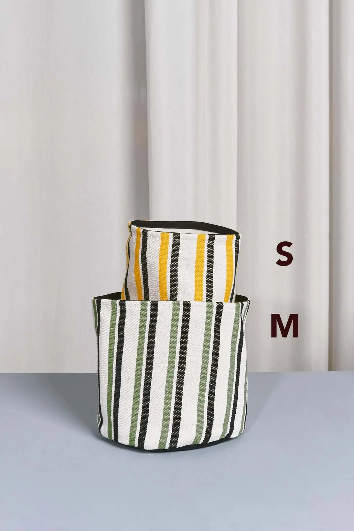 Dos cestos cilíndricos de loneta a rayas verticales: uno amarillo y otro verde, con bordes negros. Tallas S y M.