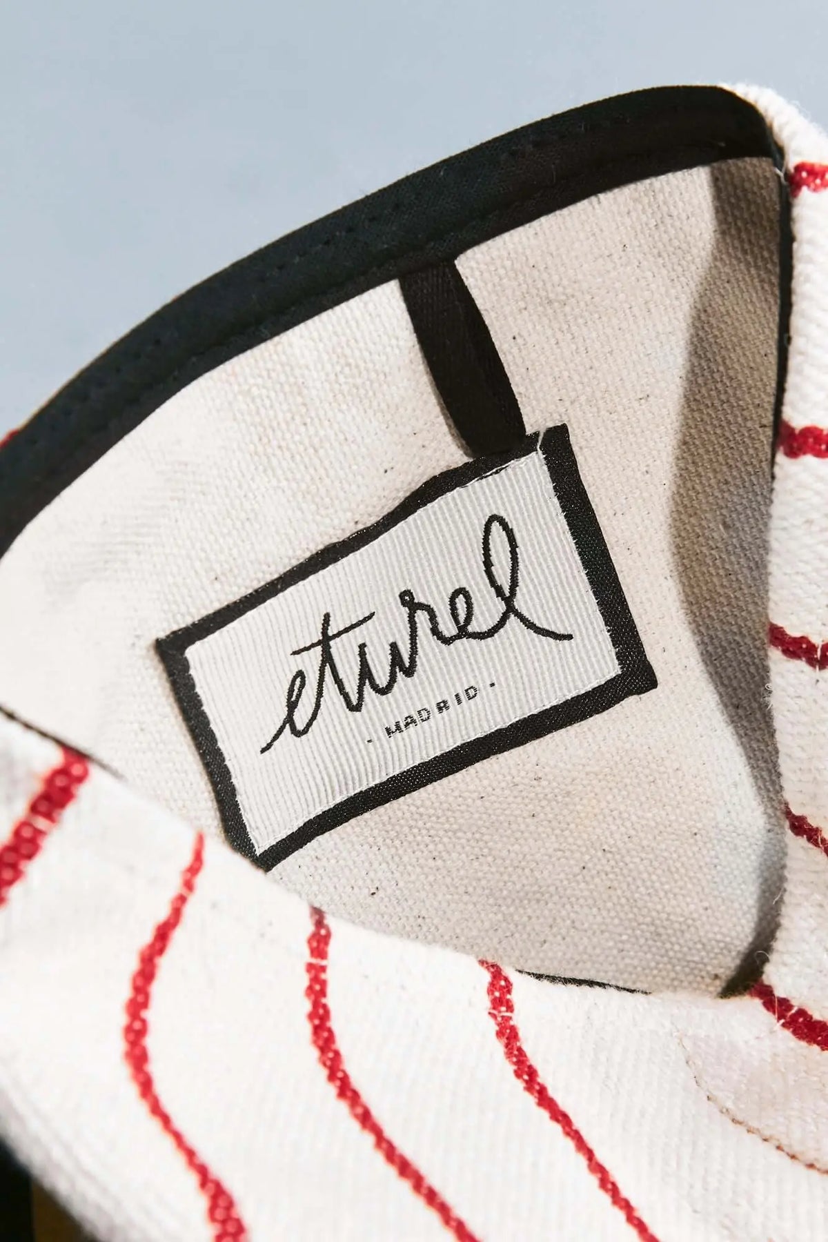 Close-up of a white artisanal basket with maroon stripes and an interior label reading "eturel MADRID."