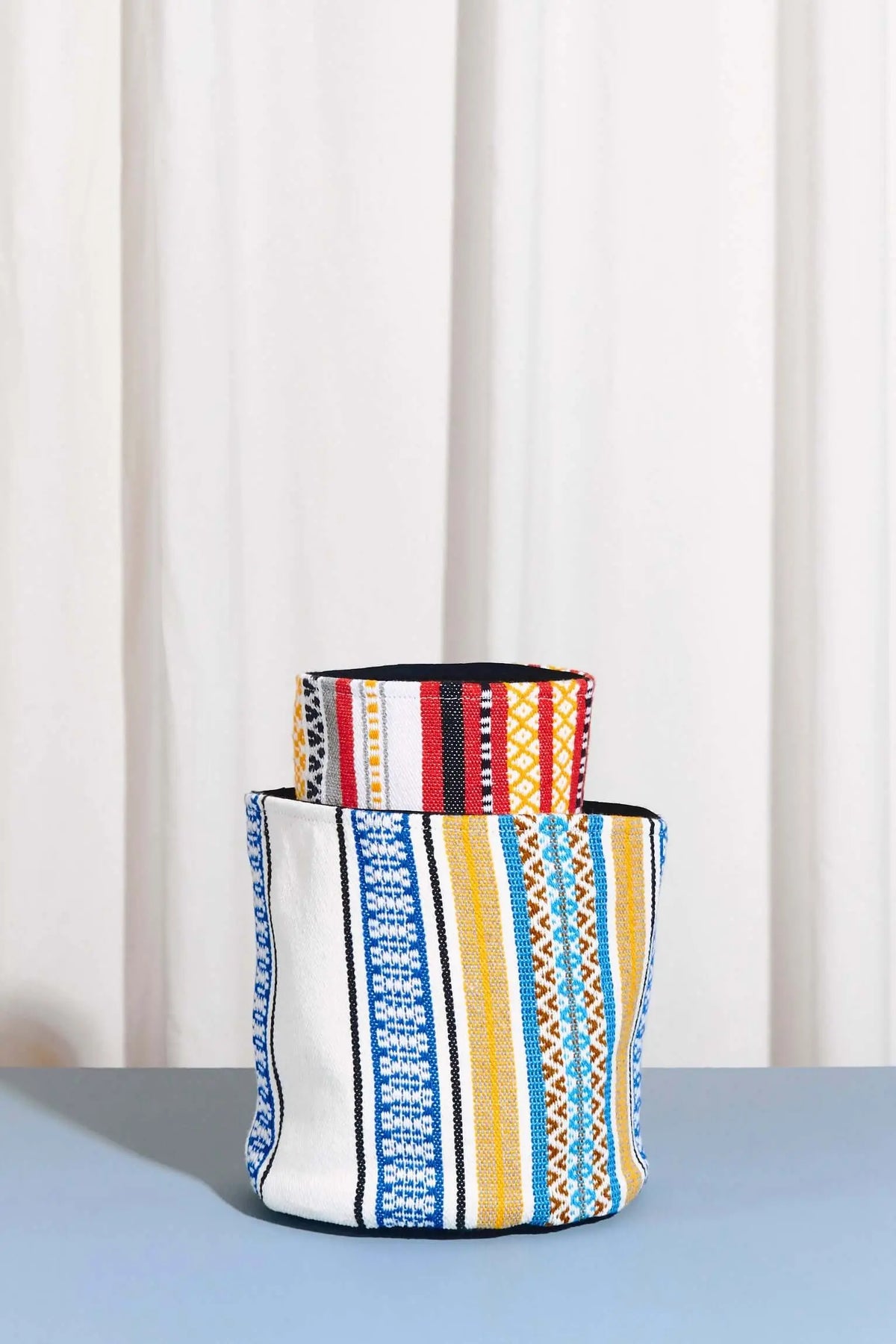 Cesto artesanal de tejido multicolor con patrones geométricos y franjas en azul, rojo, amarillo y blanco.