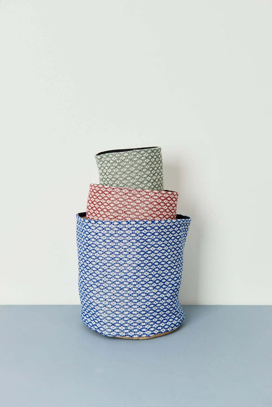 Tres cestos de tela apilados con tejido estampado ojo de perdiz en tonos azul, granate y verde sobre fondo claro.