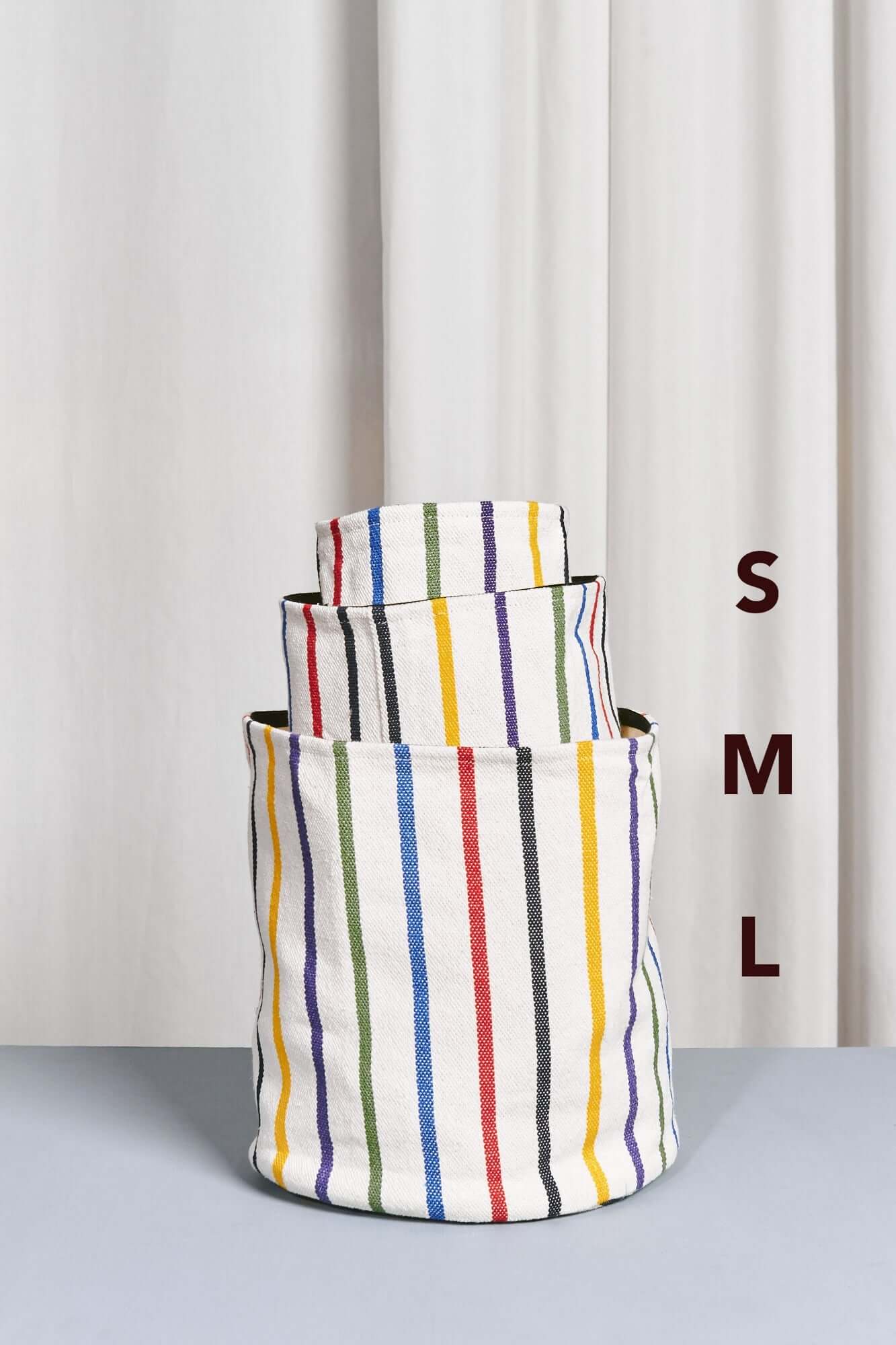 Tres cestos cilíndricos de tela blanca con rayas verticales multicolores, apilados de mayor a menor tamaño.