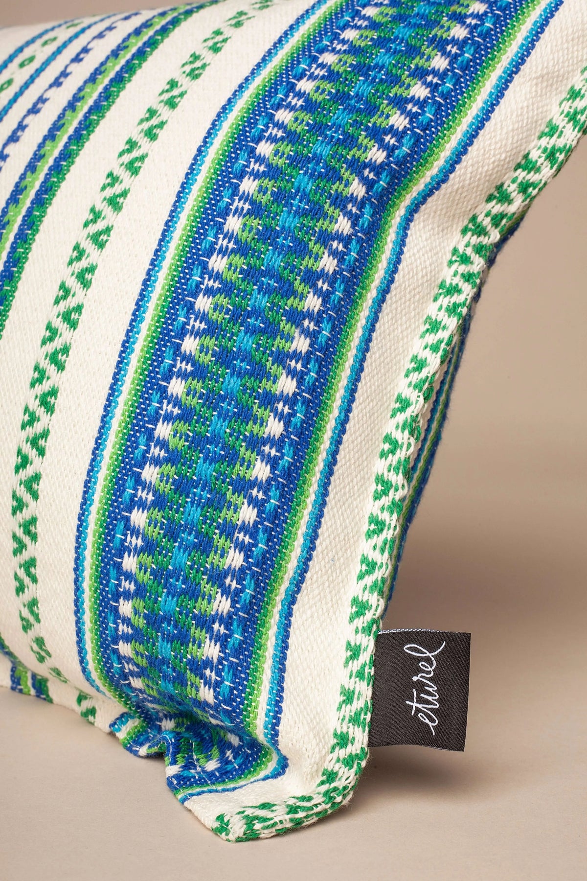 Funda de cojín con tejido manchego en tonos verde y azul sobre fondo blanco, de estilo artesanal y textura natural.
