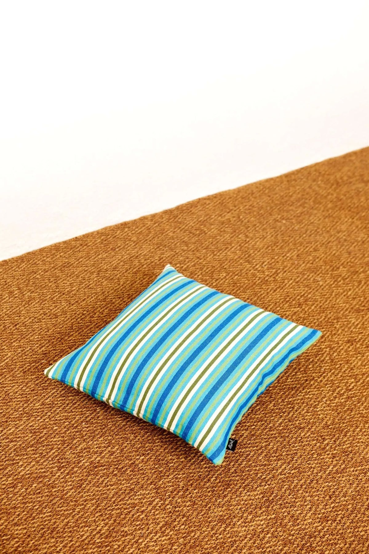 Cojín cuadrado de 50x50 cm con estampado de rayas azules, verdes y blancas sobre fondo de fibra natural.