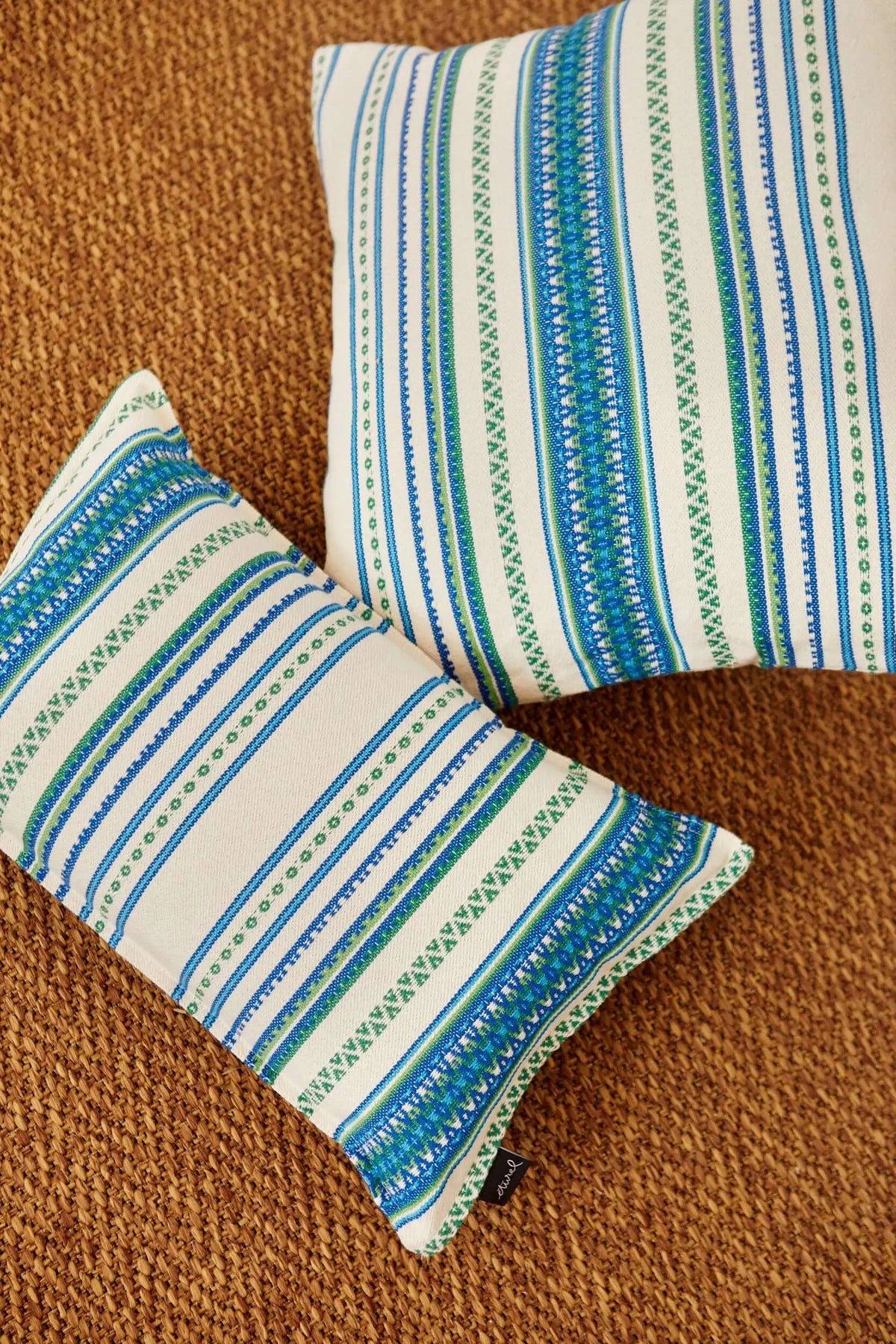 Dos fundas de cojín de tejido artesanal con rayas verticales en tonos verdes y azules sobre fondo de algodón natural.