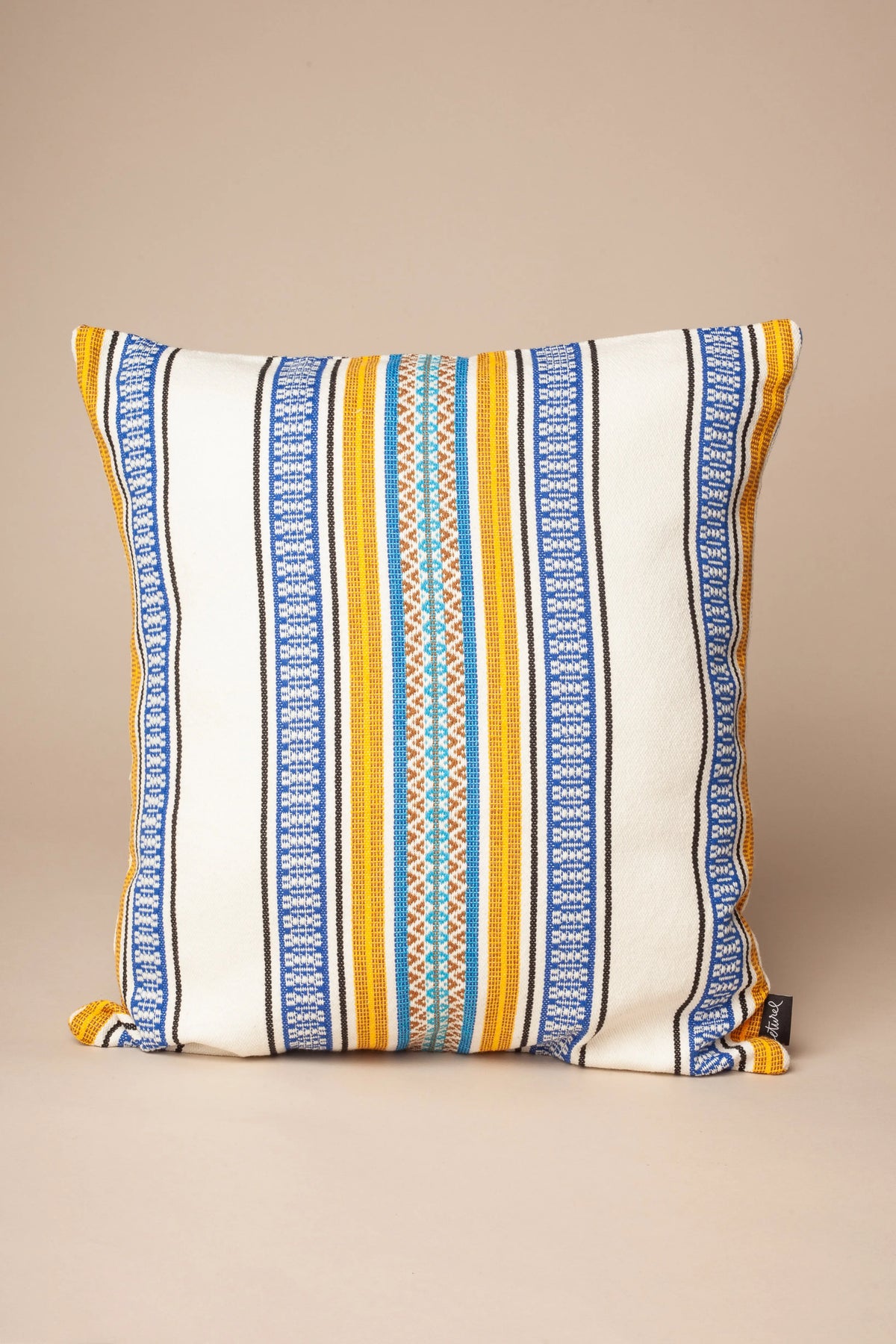 Cojín cuadrado de algodón blanco con rayas azules, amarillas y detalles en turquesa, estilo boho chic.