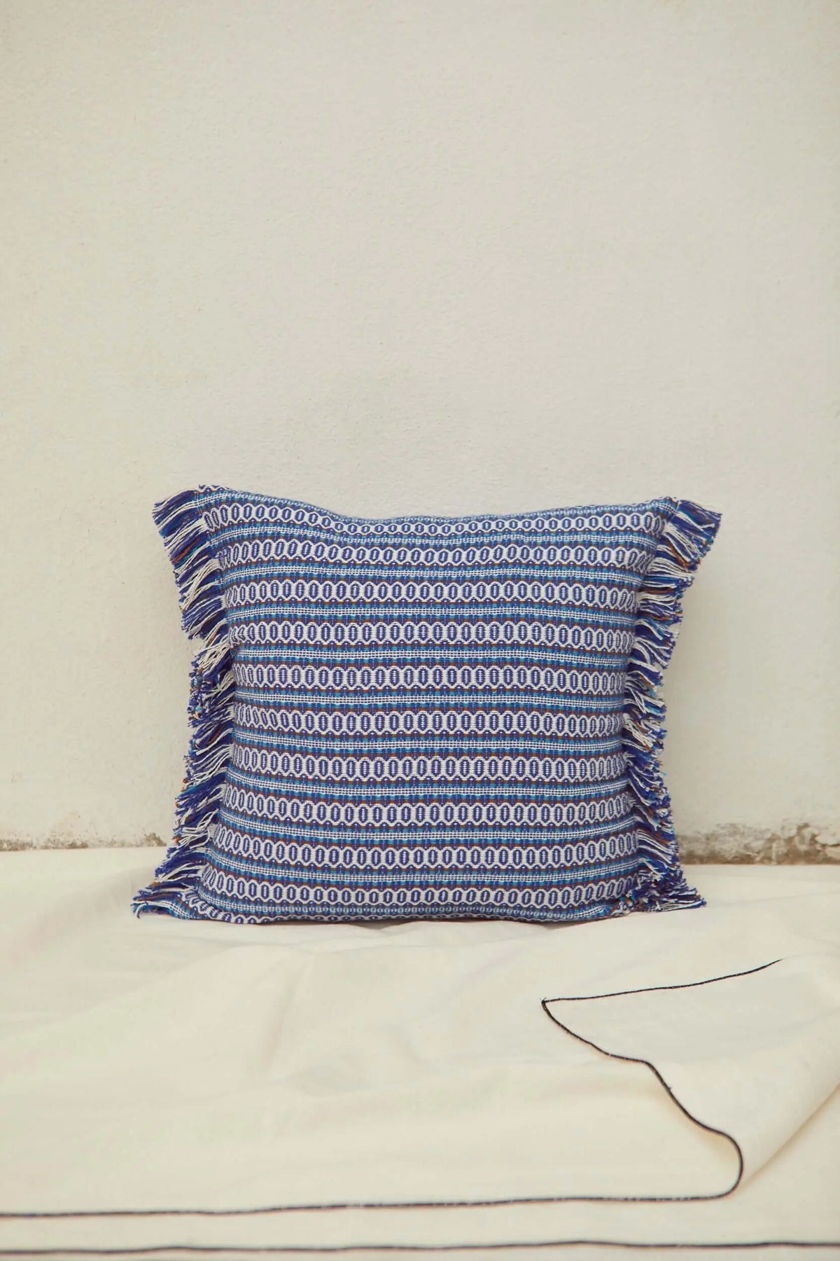 Funda de cojín azul con estampado geométrico tipo ojo de perdiz, estilo retro y bordes decorados con flecos.