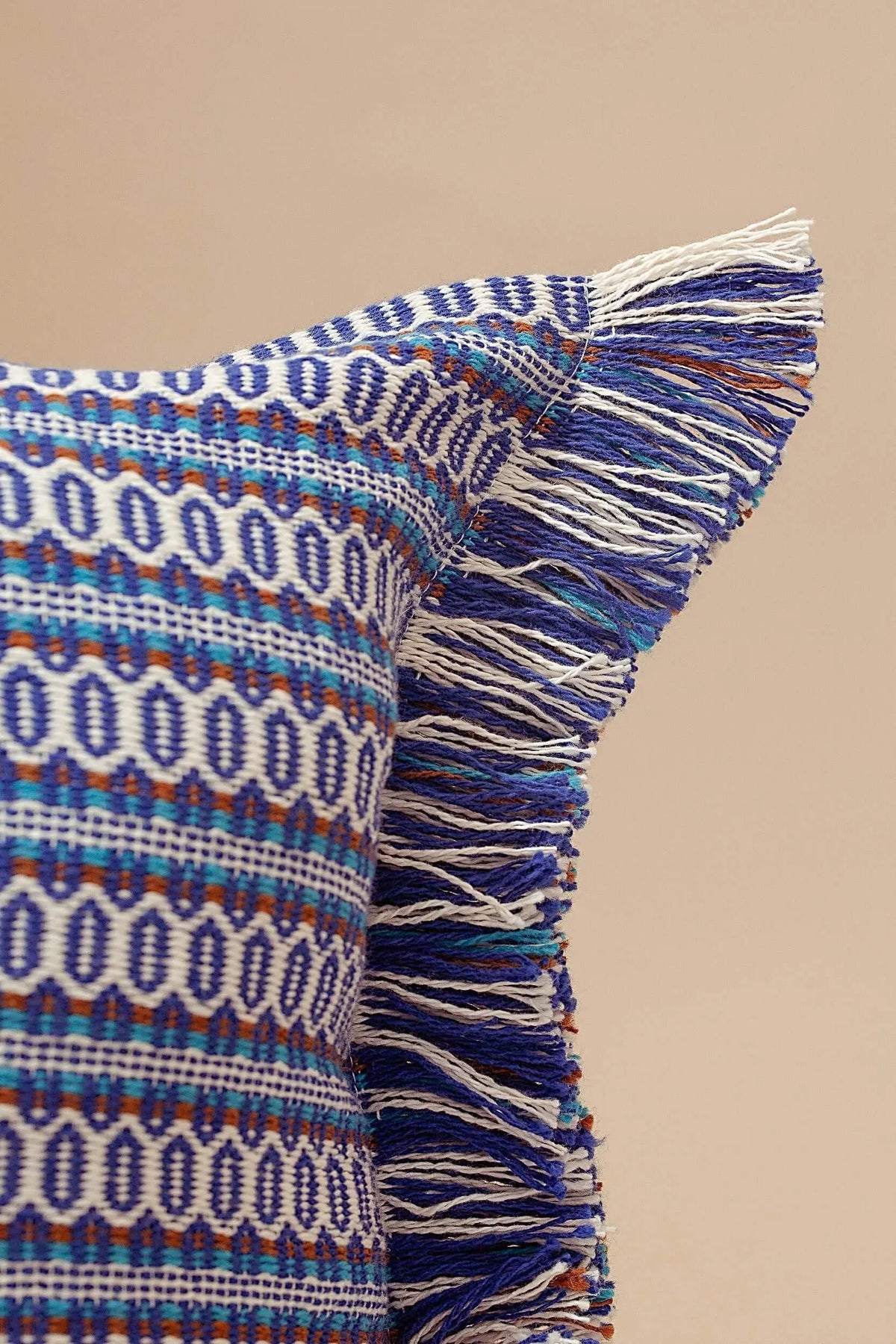 Funda de cojín azul con patrón geométrico estilo retro, textura tejida y flecos decorativos en los bordes.