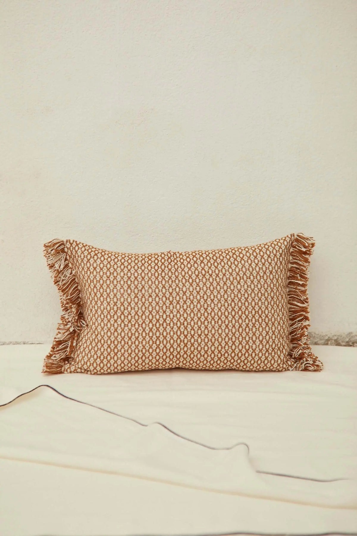 Funda de cojín rectangular color caramelo, estampado ojo de perdiz, con flecos en los extremos. Estilo artesanal.