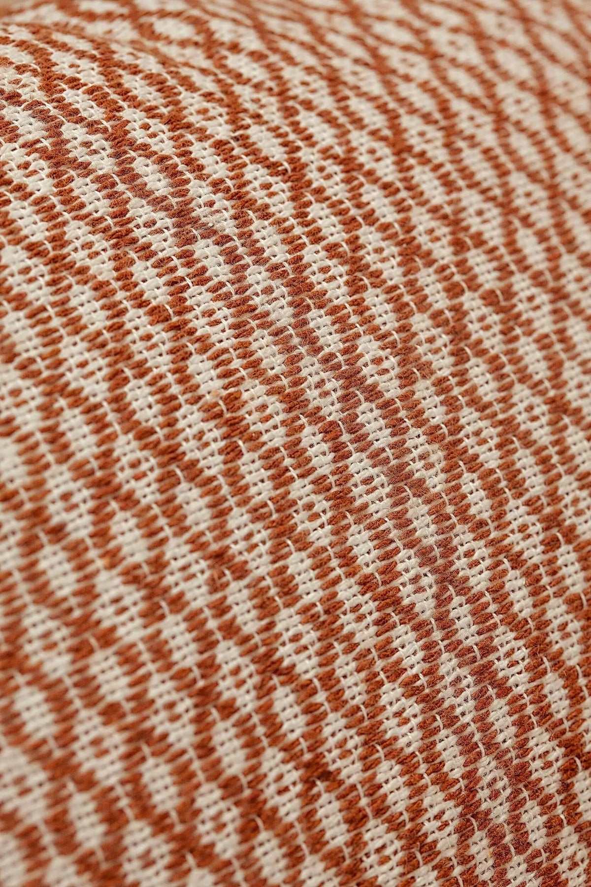 Close-up of a caramel and cream-colored cushion cover with a textured, woven houndstooth-style pattern.