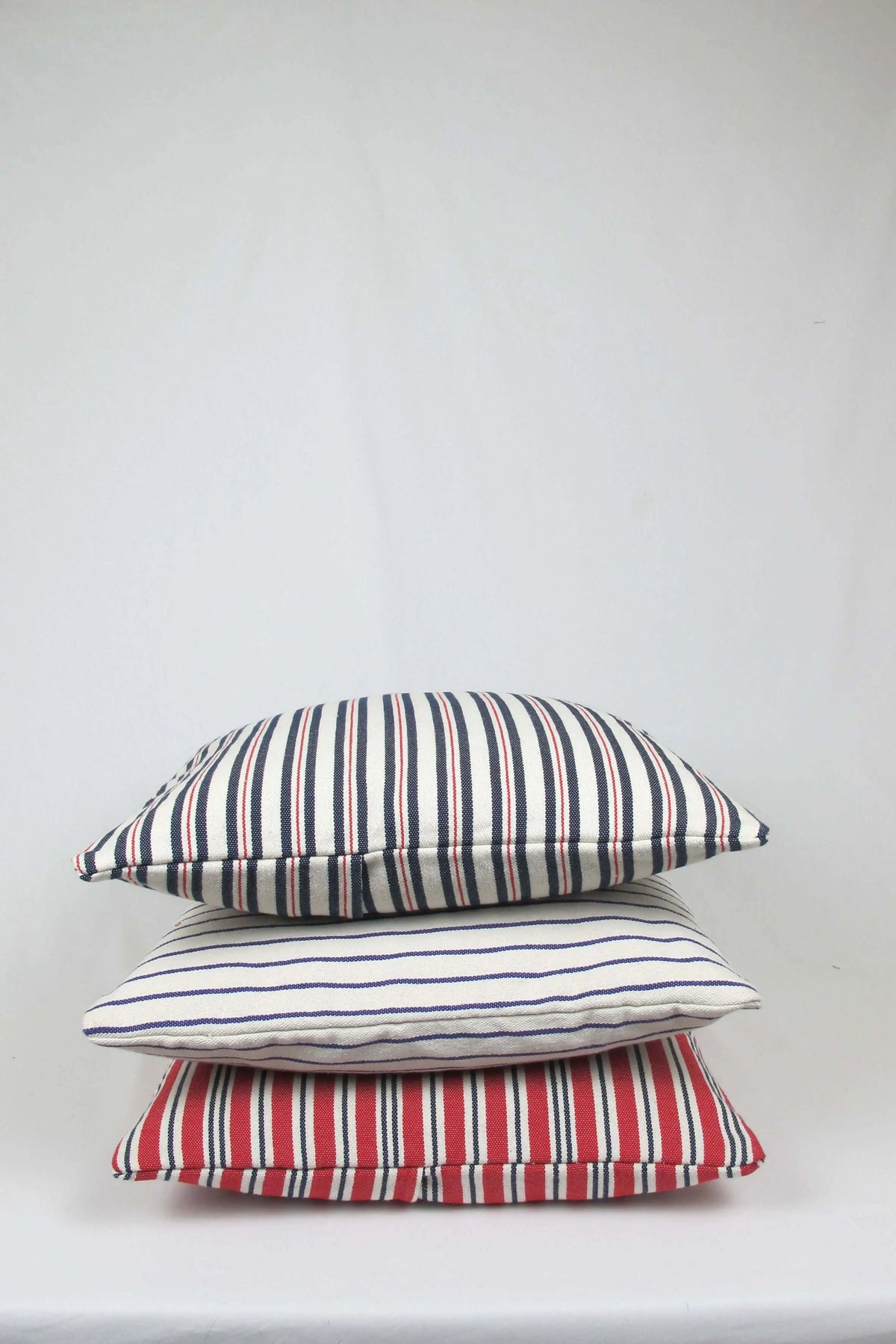 Pila de tres fundas de cojín de loneta 45x45 cm con diseño a rayas verticales y horizontales en azul, rojo y crema.