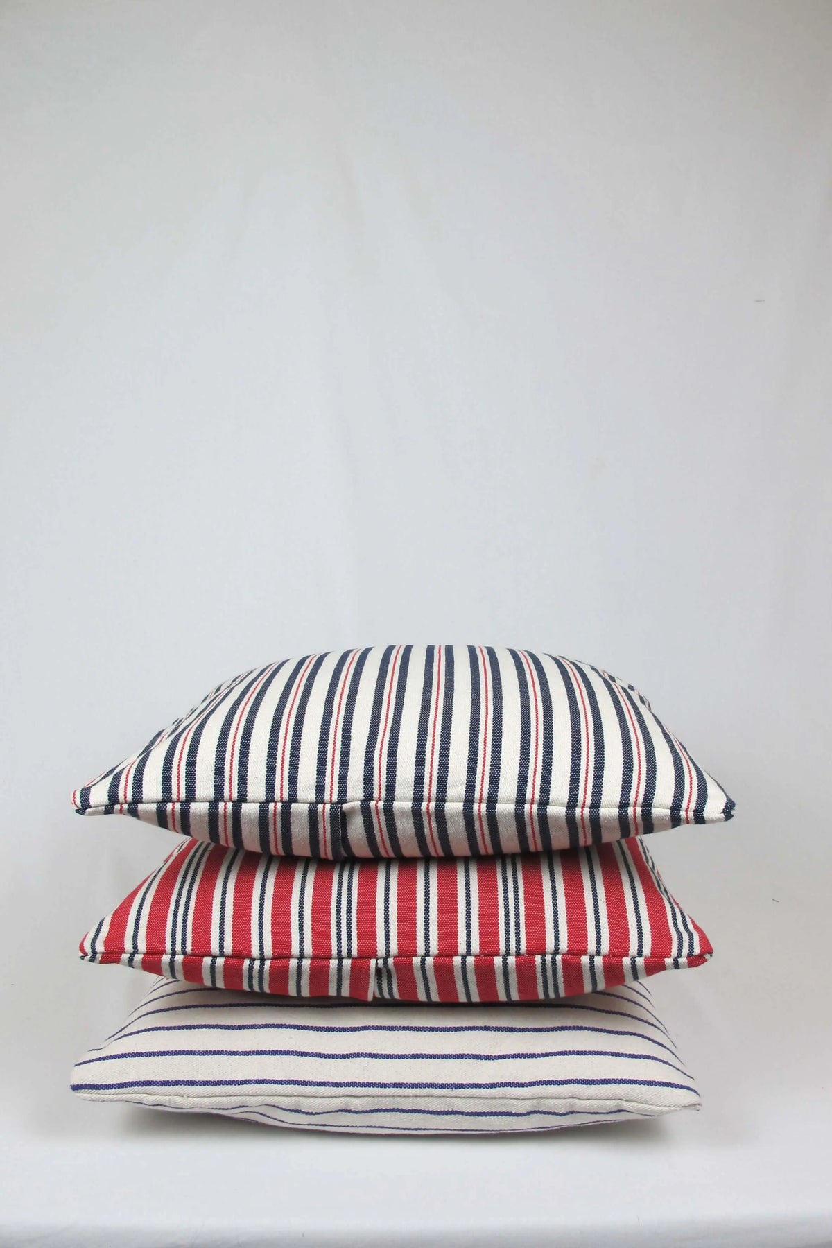 Pila de tres cojines de loneta cuadrados de 45x45 cm con diversos estampados de rayas en azul, rojo y crema.