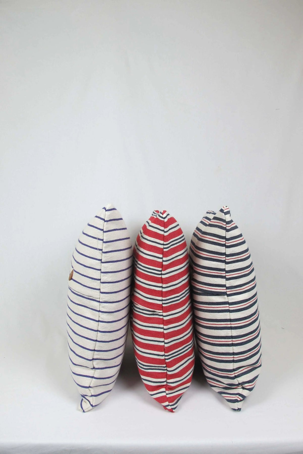 Tres fundas de cojín cuadradas de loneta con diseño de rayas en tonos azules y rojos sobre fondo claro, estilo casual.