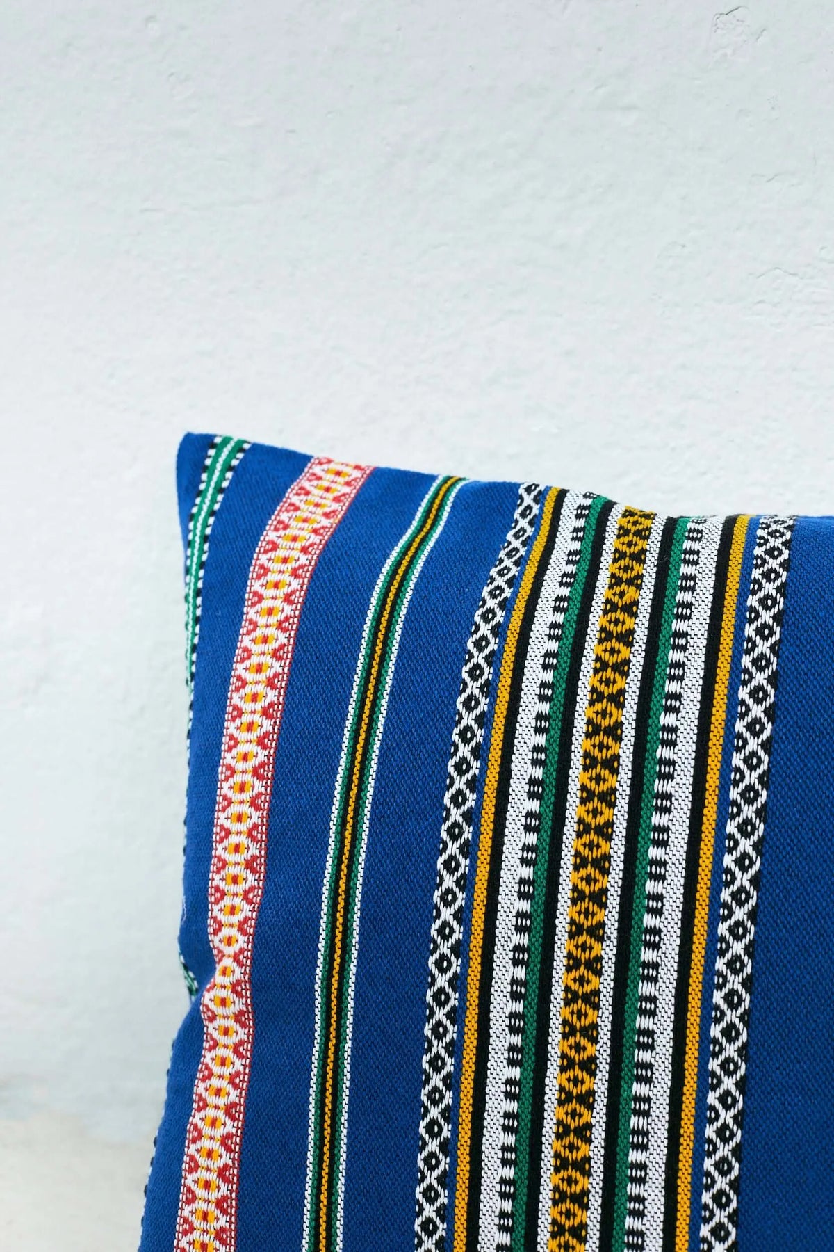 Funda de cojín azul con rayas verticales de colores y patrones geométricos estilo artesanal. 50x45cm.