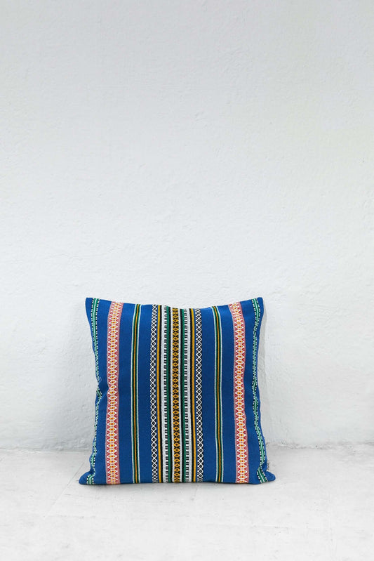 Funda de cojín azul con franjas verticales y patrones geométricos multicolores en estilo artesanal tradicional.
