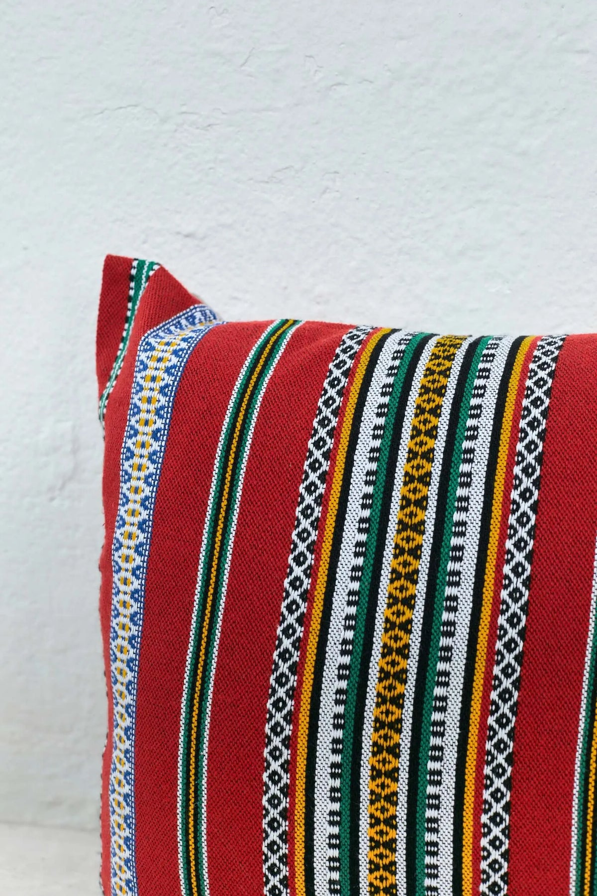 Red woven cushion cover with vibrant vertical stripes in yellow, green, blue, black, and white geometric patterns.