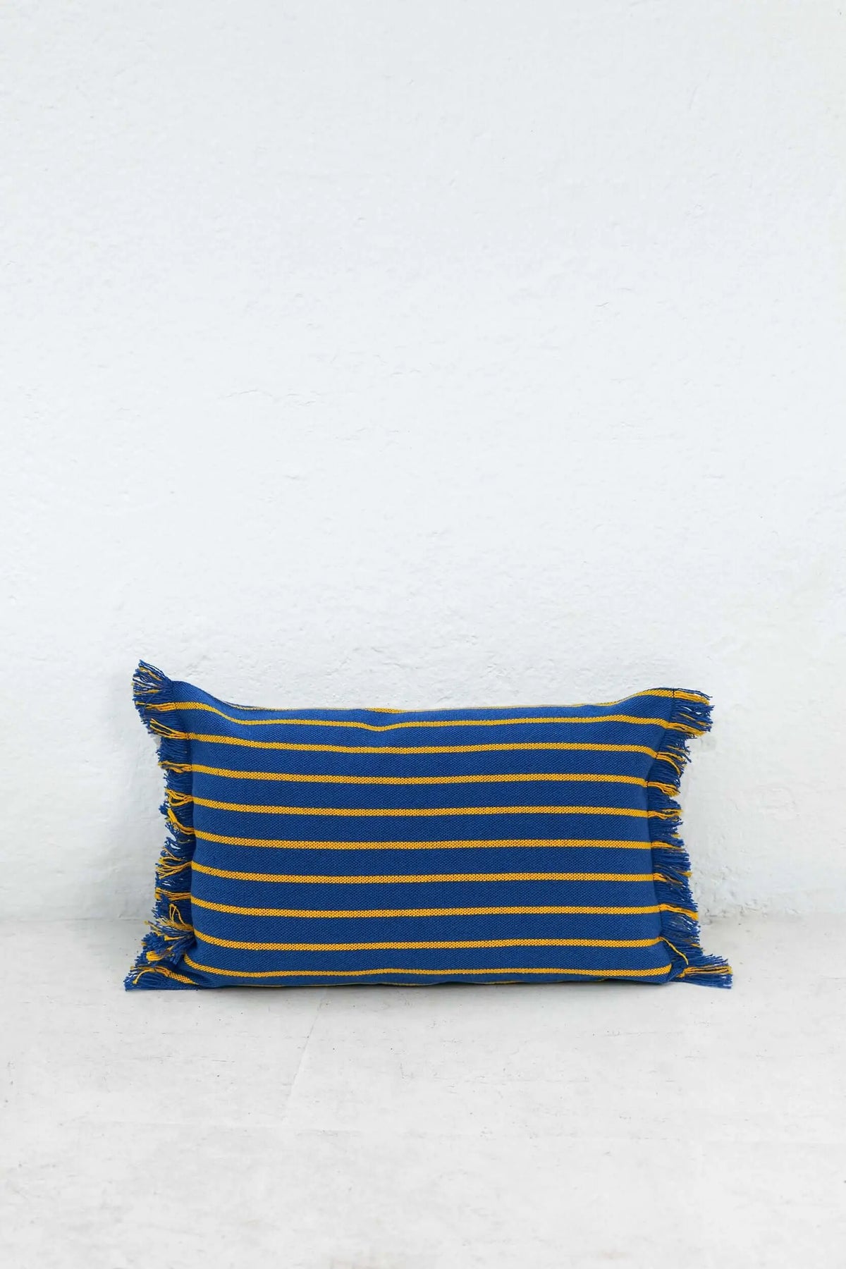 Funda de cojín rectangular azul con rayas horizontales amarillas y flecos laterales, estilo decorativo y textil.