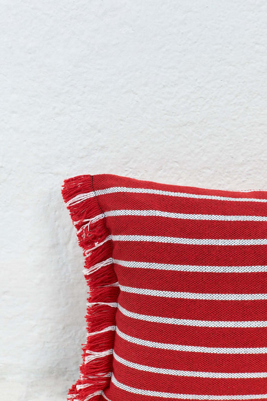 Funda de cojín rectangular a rayas rojas y blancas con textura tejida y flecos decorativos en un lateral.