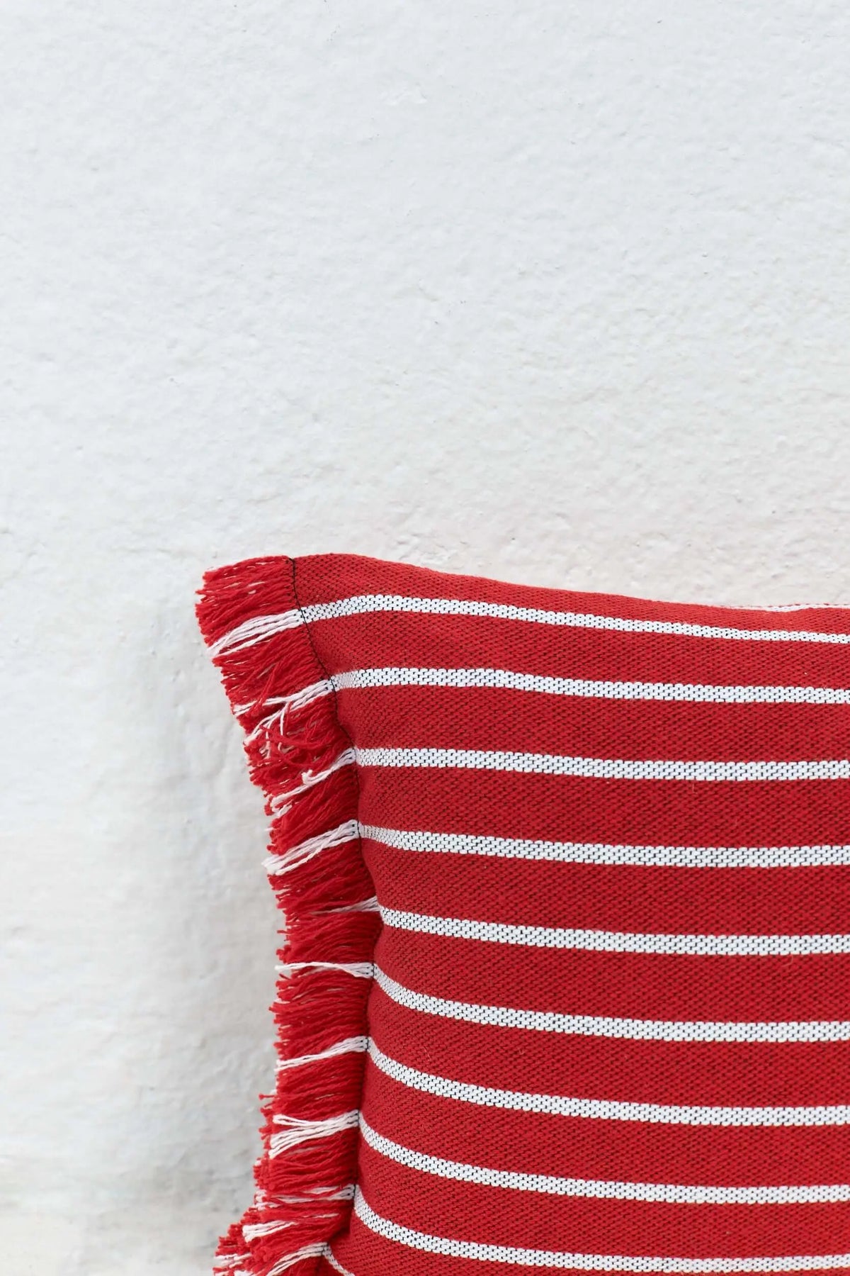 Funda de cojín rectangular a rayas rojas y blancas con textura tejida y flecos decorativos en un lateral.