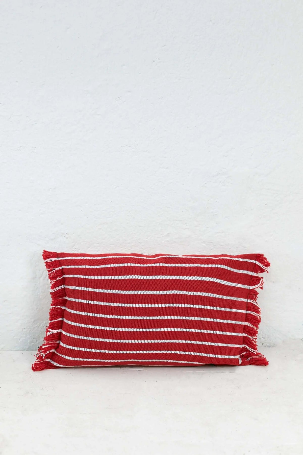 Funda de cojín rectangular 30x45cm, tejido a rayas rojas y blancas con detalles de flecos en los extremos laterales.
