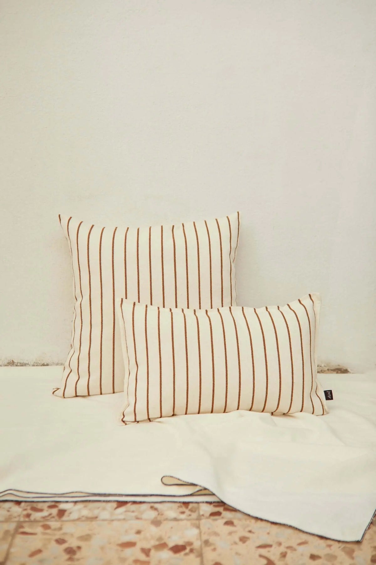 Dos fundas de cojín de loneta color crema con rayas verticales finas en color caramelo, estilo rústico y minimalista.