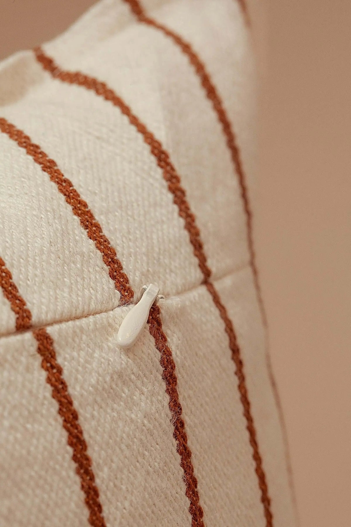 Close-up of a cream-colored canvas cushion cover with textured rust-brown vertical stripes and a hidden zipper.