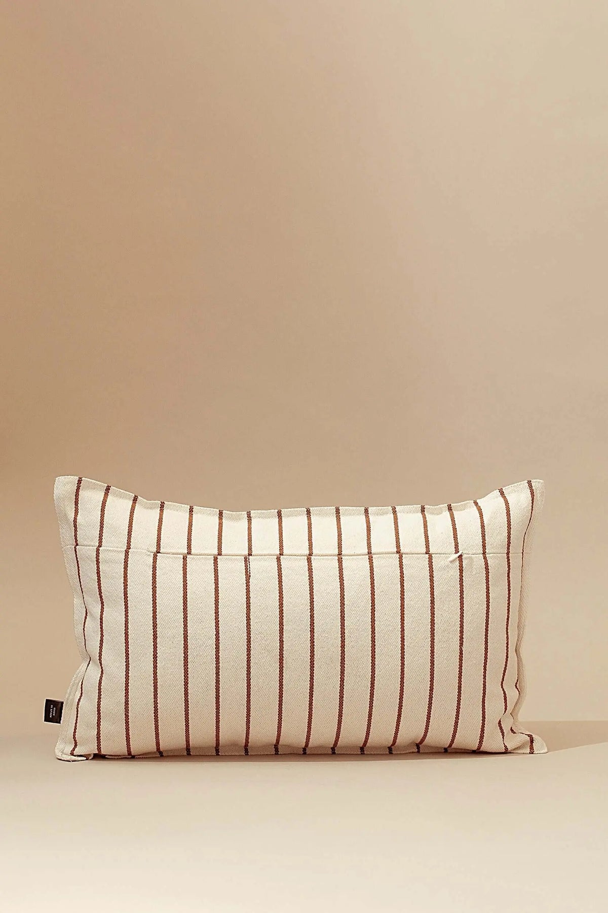 Rectangular canvas cushion cover with vertical brown stripes on an off-white background against a beige backdrop.
