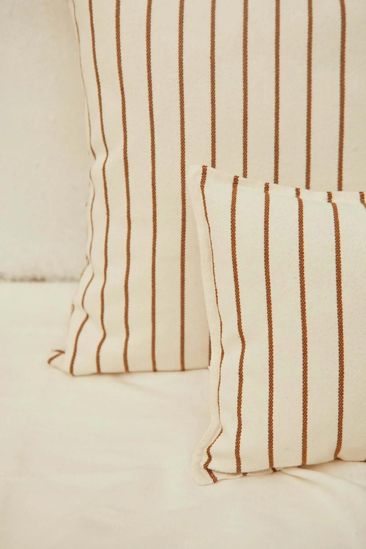 Funda de cojín en loneta color crema con diseño de finas rayas verticales en tono caramelo, estilo natural y minimalista.