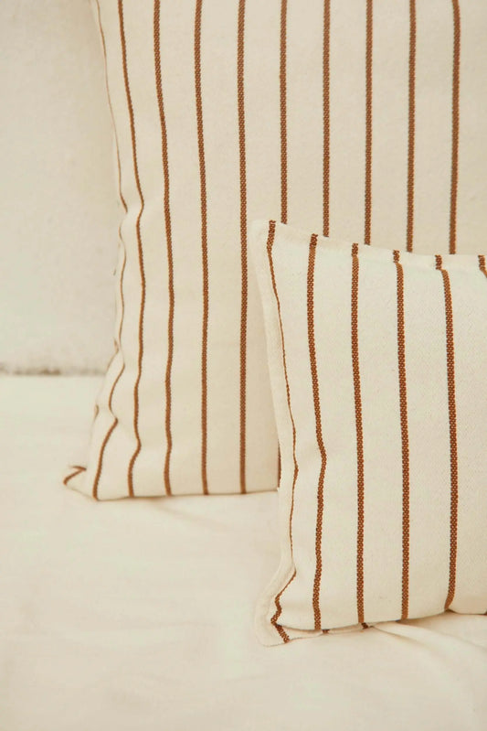 Funda de cojín en loneta color crema con diseño de finas rayas verticales en tono caramelo, estilo natural y minimalista.