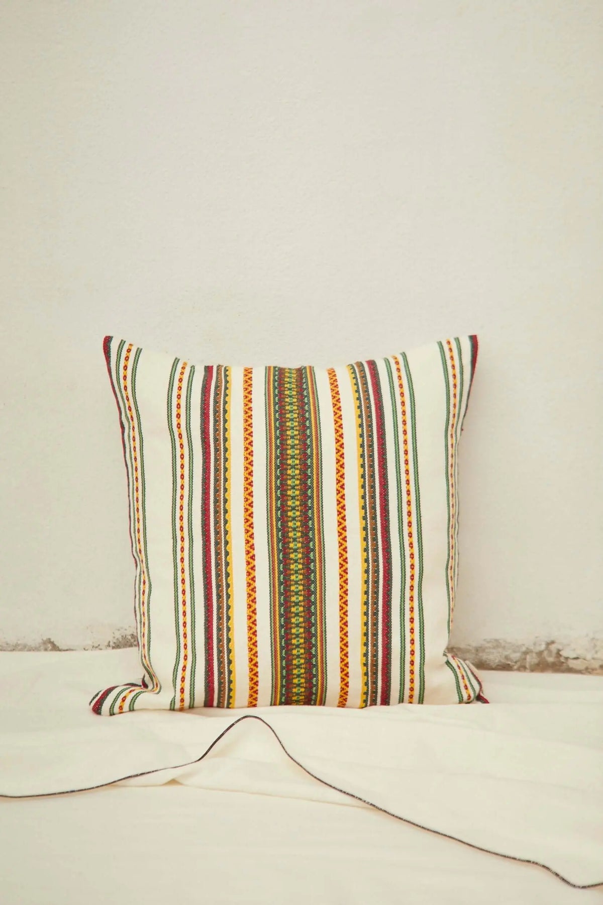 Square cushion in cream fabric with a colorful, traditional Manchego-style vertical striped pattern.
