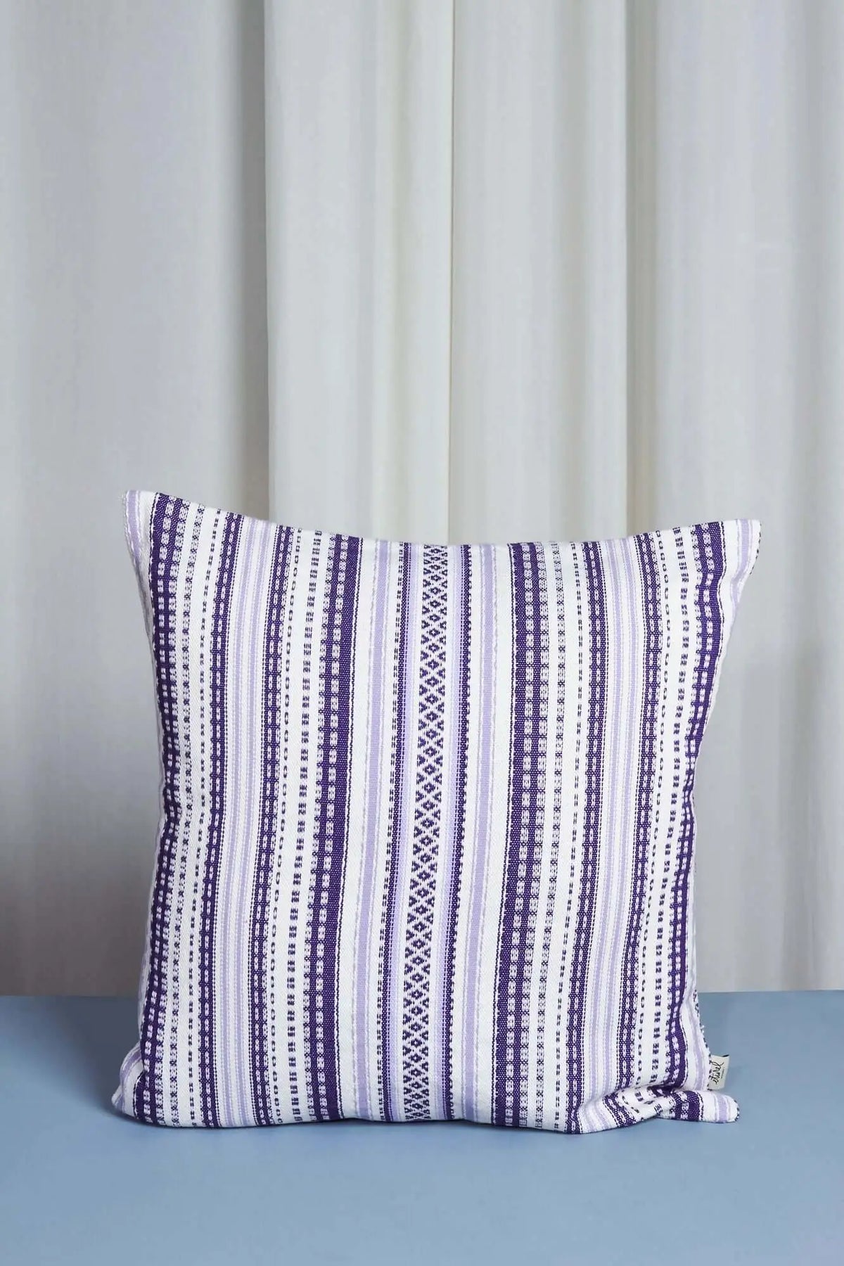 Funda de cojín de estilo alpujarreño en tonos malva y blanco con patrón de rayas tejidas, medida 50x50 cm.