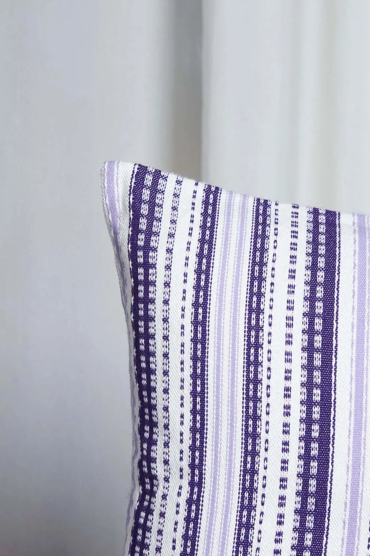Funda de cojín 50x50 cm estilo alpujarreño, tejido de rayas verticales en tonos morado y malva sobre fondo blanco.
