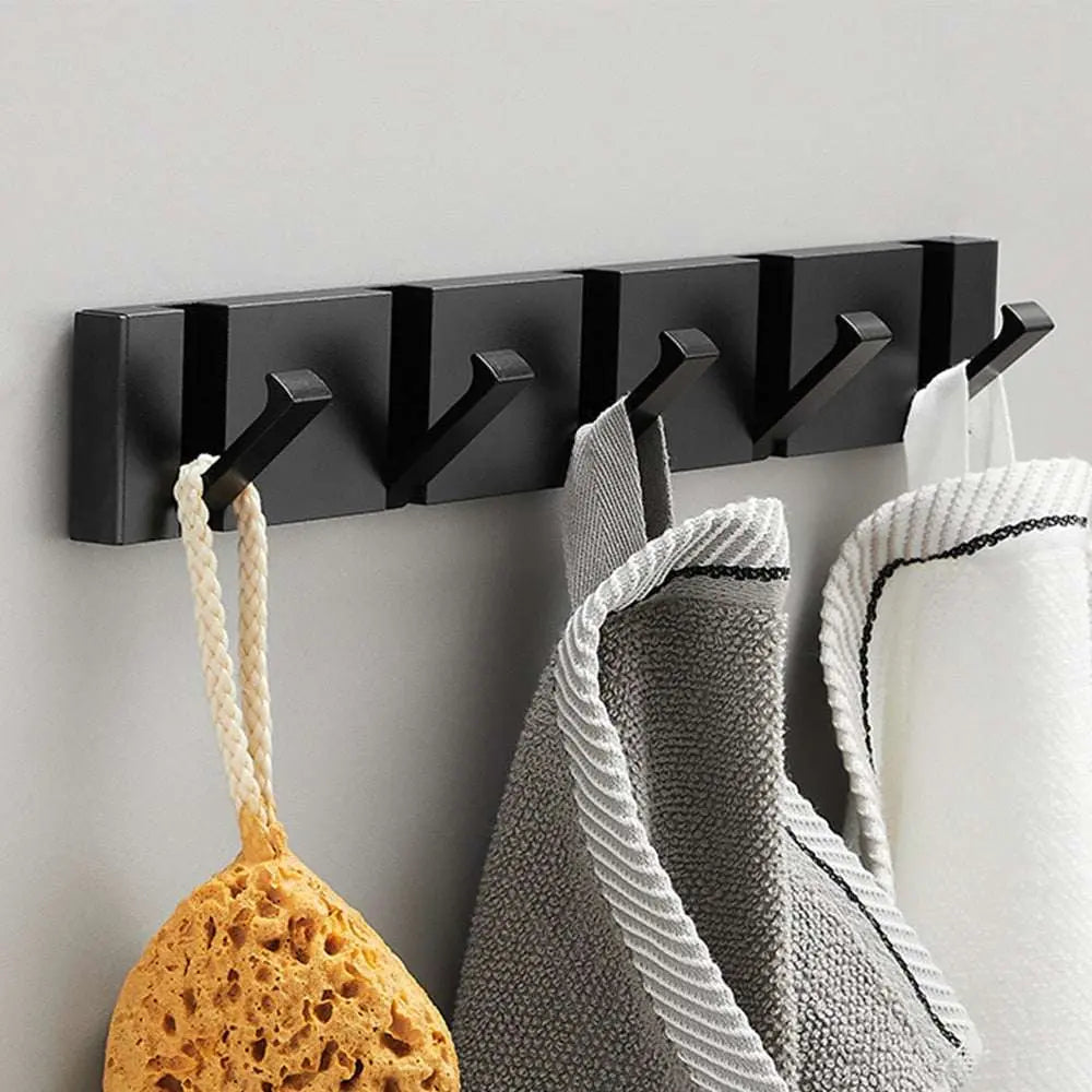 Perchero de pared moderno de metal negro con ganchos plegables, sosteniendo esponjas y toallas sobre fondo gris claro.