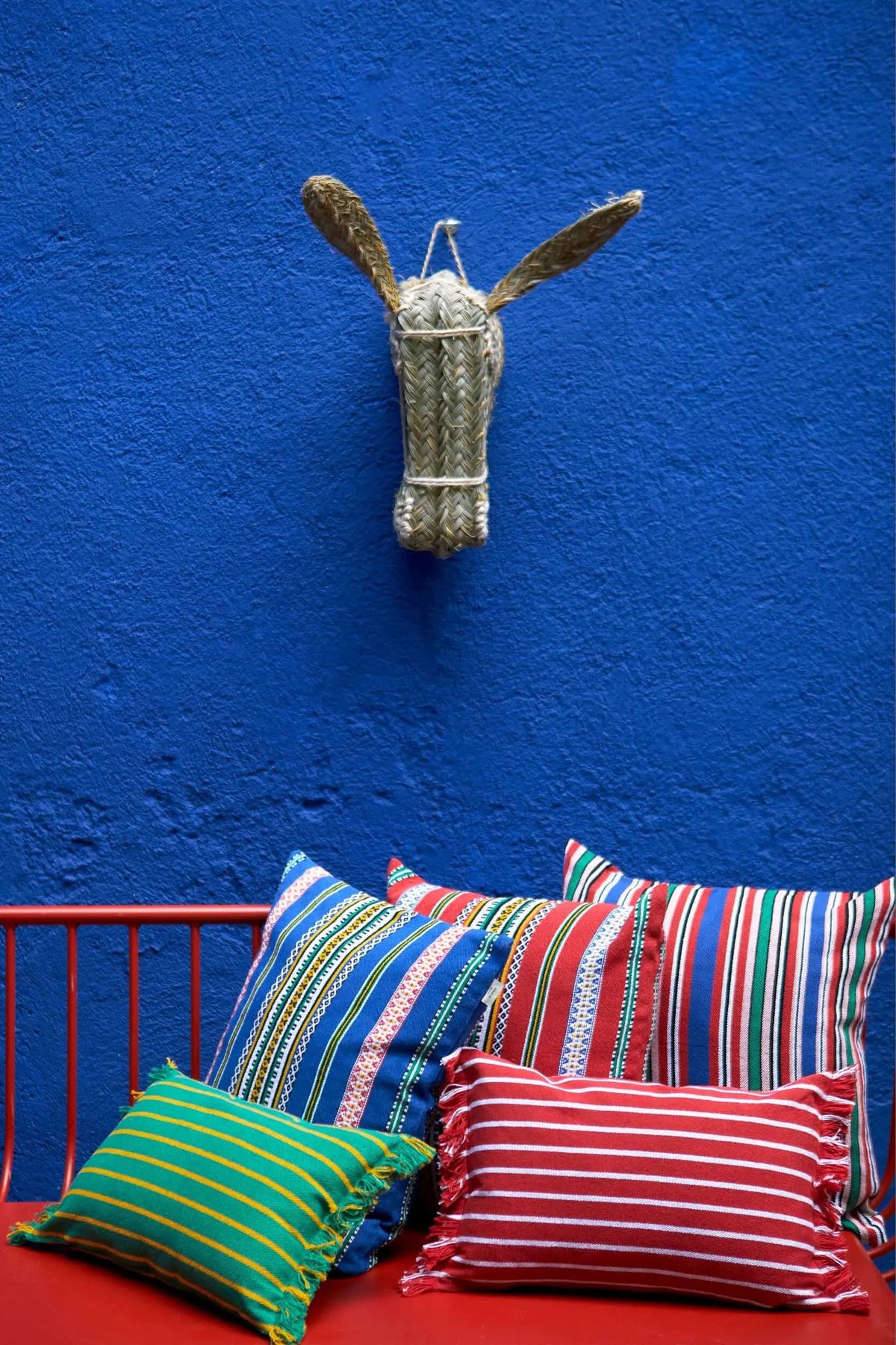 Rectangular red cushion with white stripes and frayed edges, displayed with other vibrant striped pillows.
