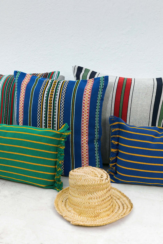 Funda de cojín rectangular verde con rayas amarillas y flecos laterales, estilo artesanal sobre fondo blanco.