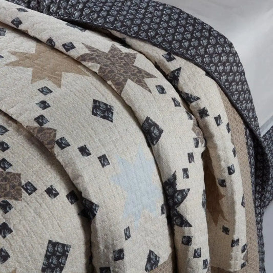 Quilted bedding featuring tan and dark brown star patterns with small geometric accents and a floral border.