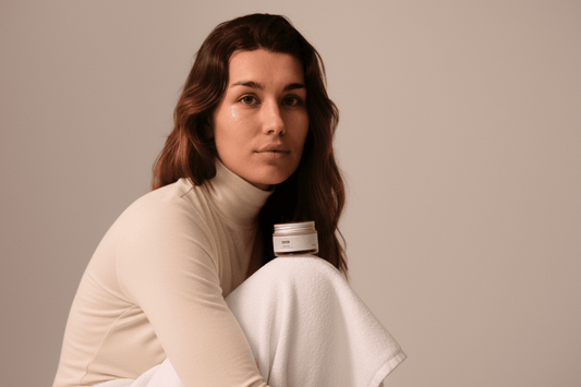 Mujer de piel natural sostiene un tarro de crema facial Banbu Moon con tapa metálica sobre un fondo neutro y suave.
