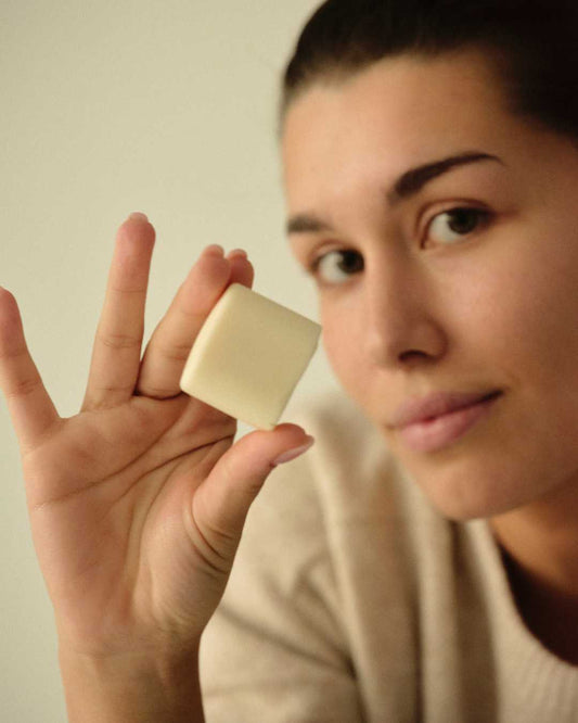 Mujer sostiene una pastilla de crema de manos sólida KUTE de Banbu, de color crema, con textura suave y acabado mate.