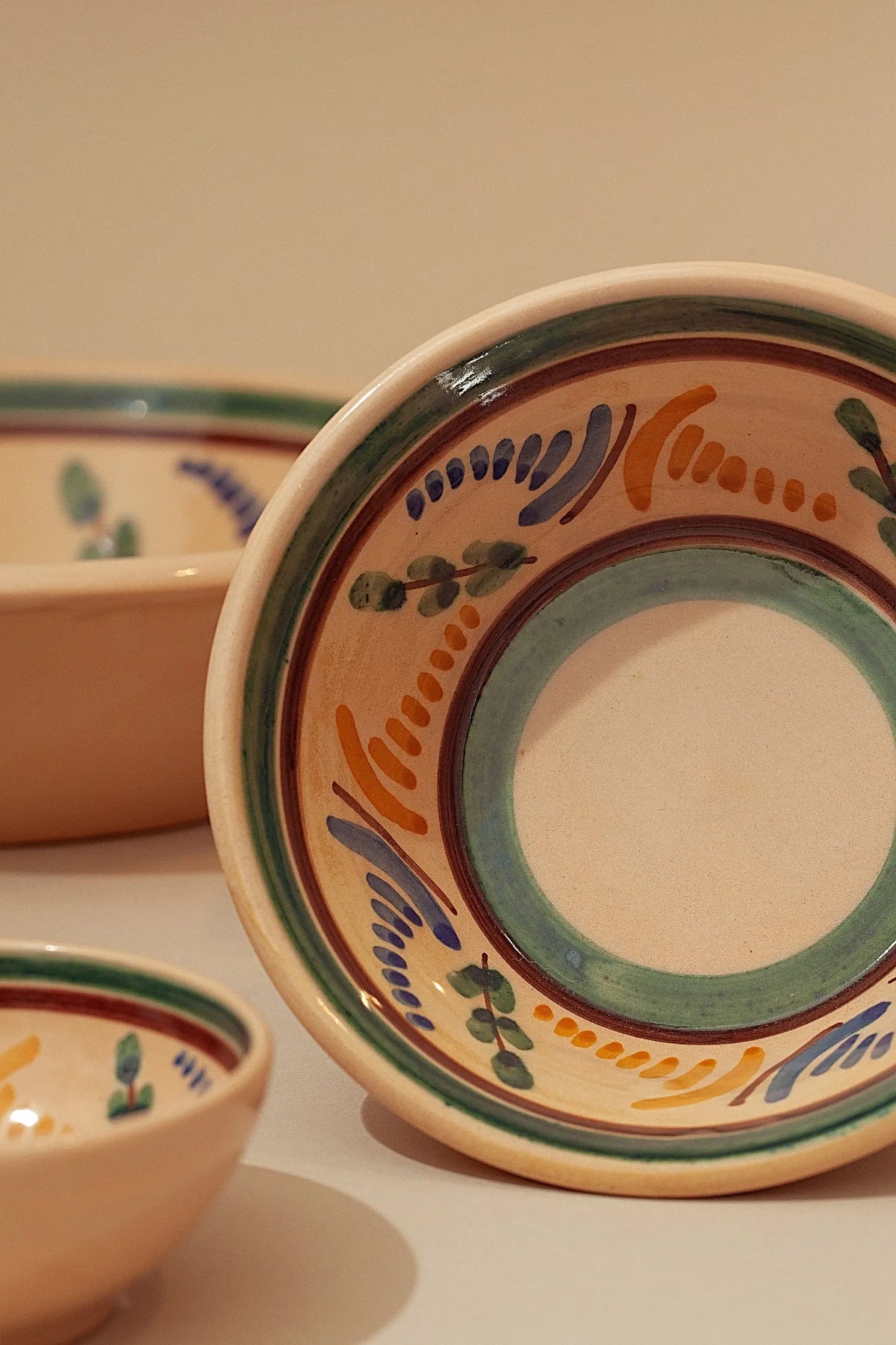 Cuencos de cerámica artesanal con motivos florales y líneas pintadas en tonos verde, azul y naranja sobre fondo crema.