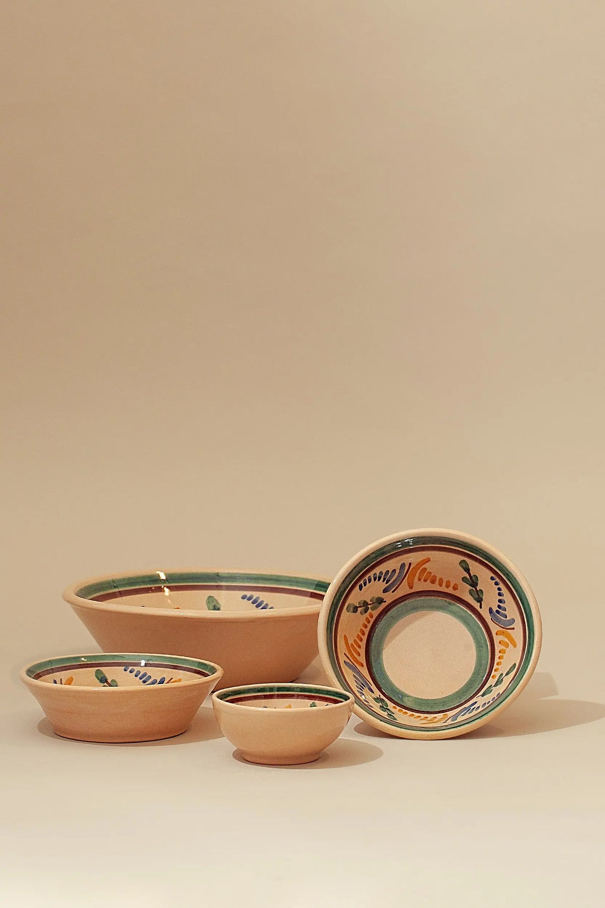 Set de cuencos de cerámica artesanal con motivos pintados a mano en tonos verde, azul y ocre sobre fondo beige claro.