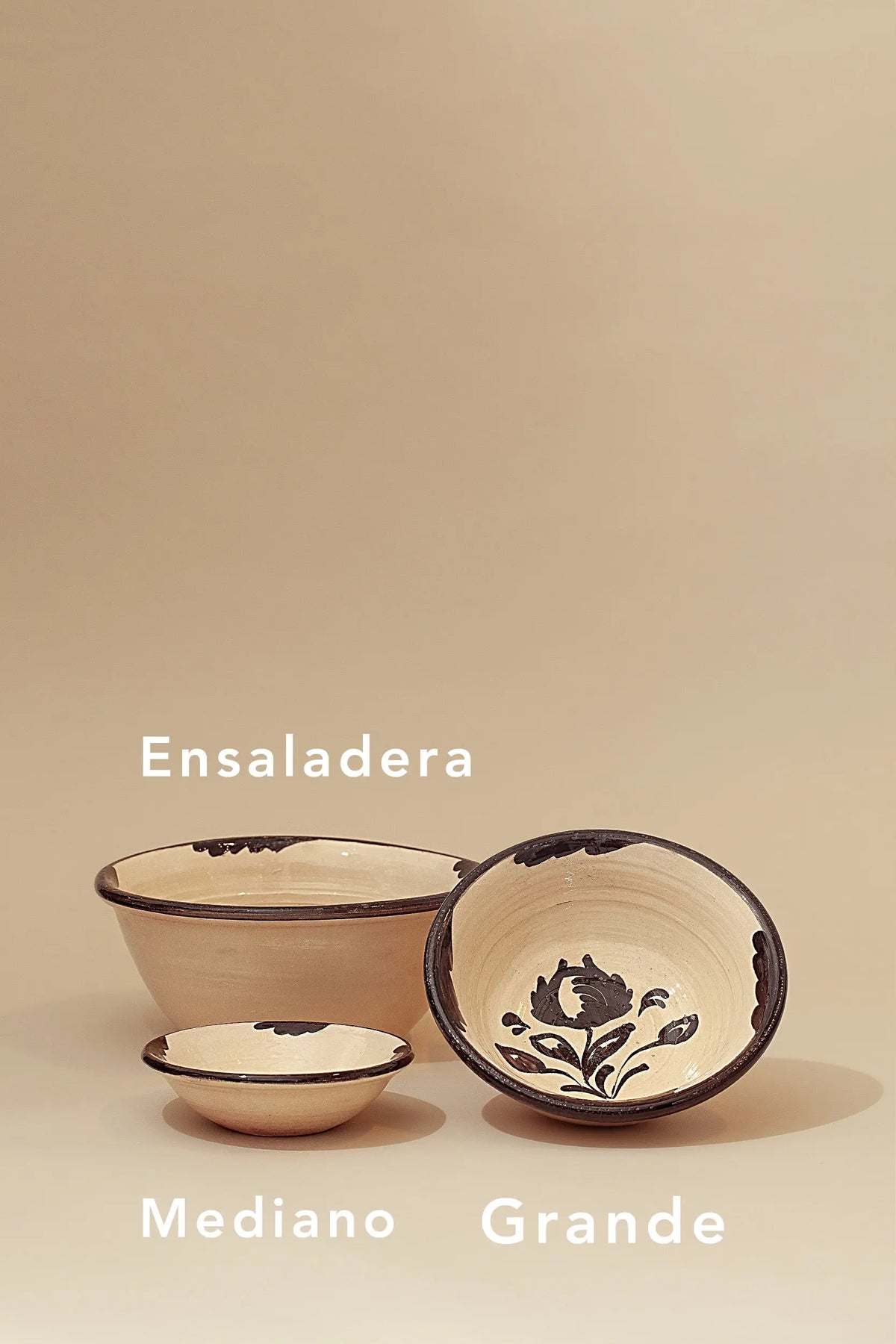 Set of three handcrafted ceramic bowls in cream with traditional black floral patterns and painted rims.