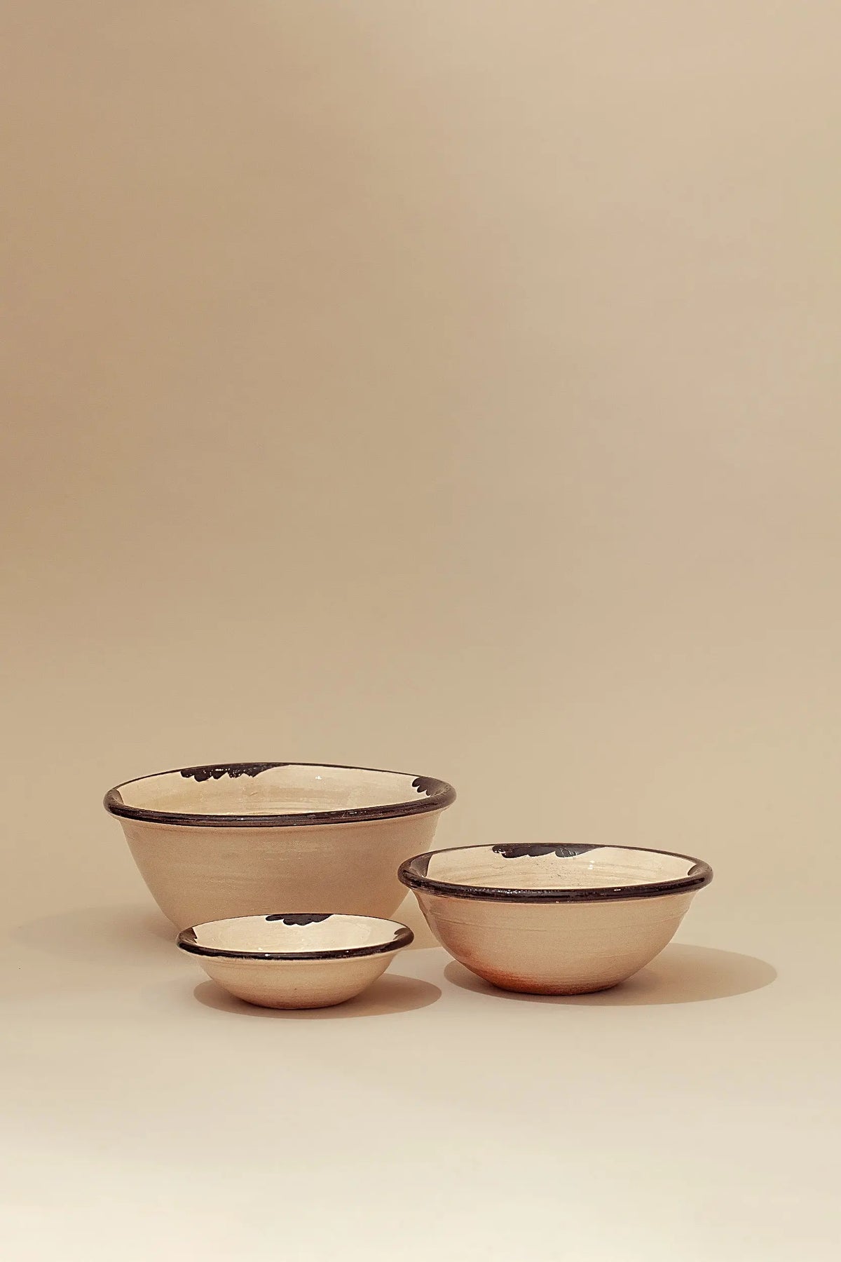 Set de tres cuencos de cerámica artesanal en color crema con detalles pintados en negro en el borde.