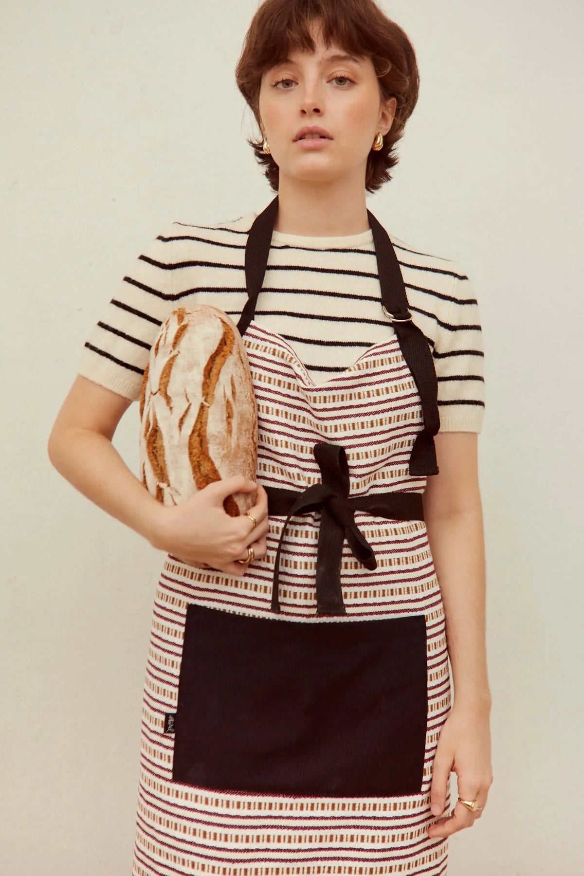 Delantal de tela tejida con rayas granate y blancas, tiras y bolsillo frontal negro, ideal para un estilo rústico.