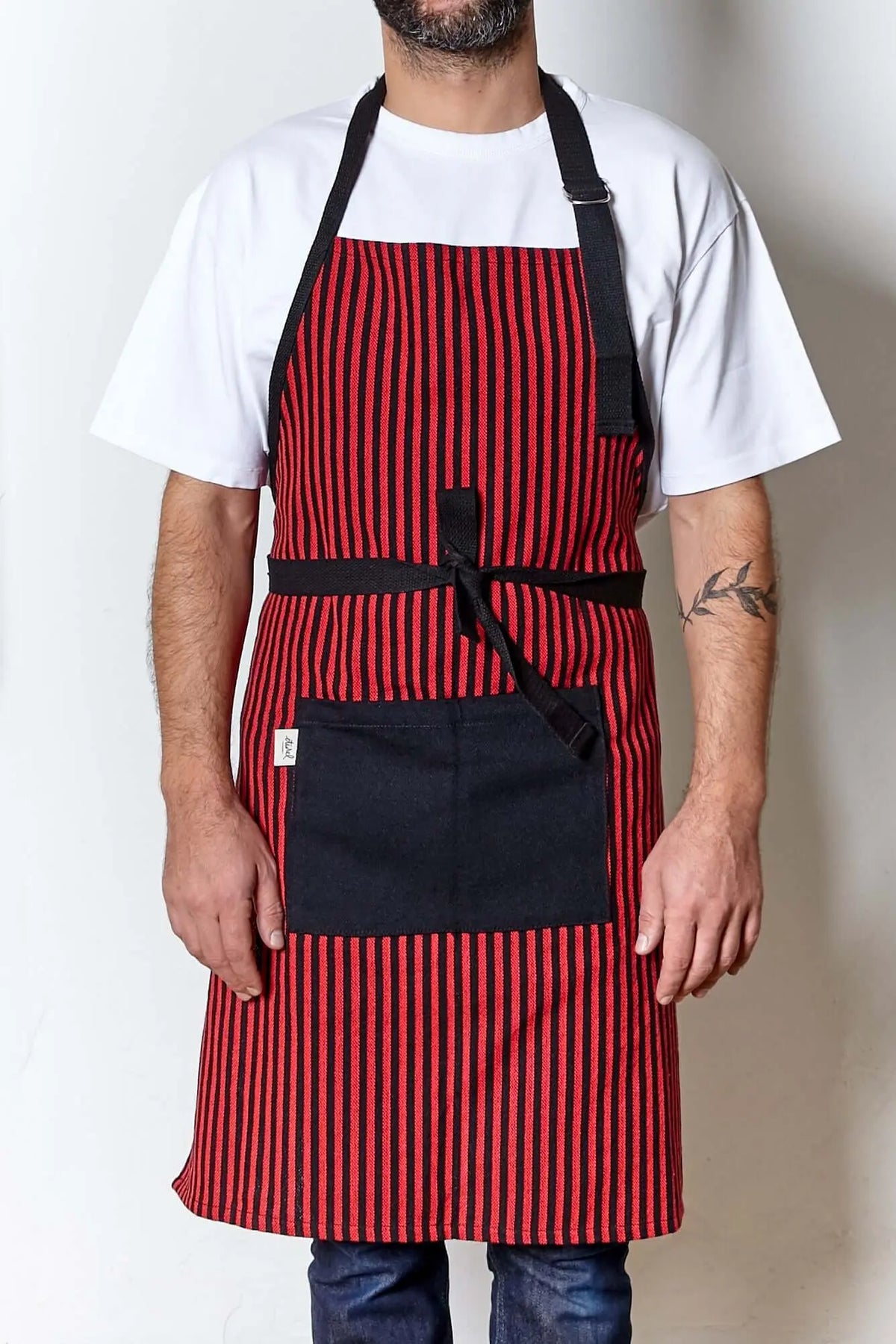 Adjustable red and black striped canvas apron with a large black front pocket and black ties, worn over a white shirt.