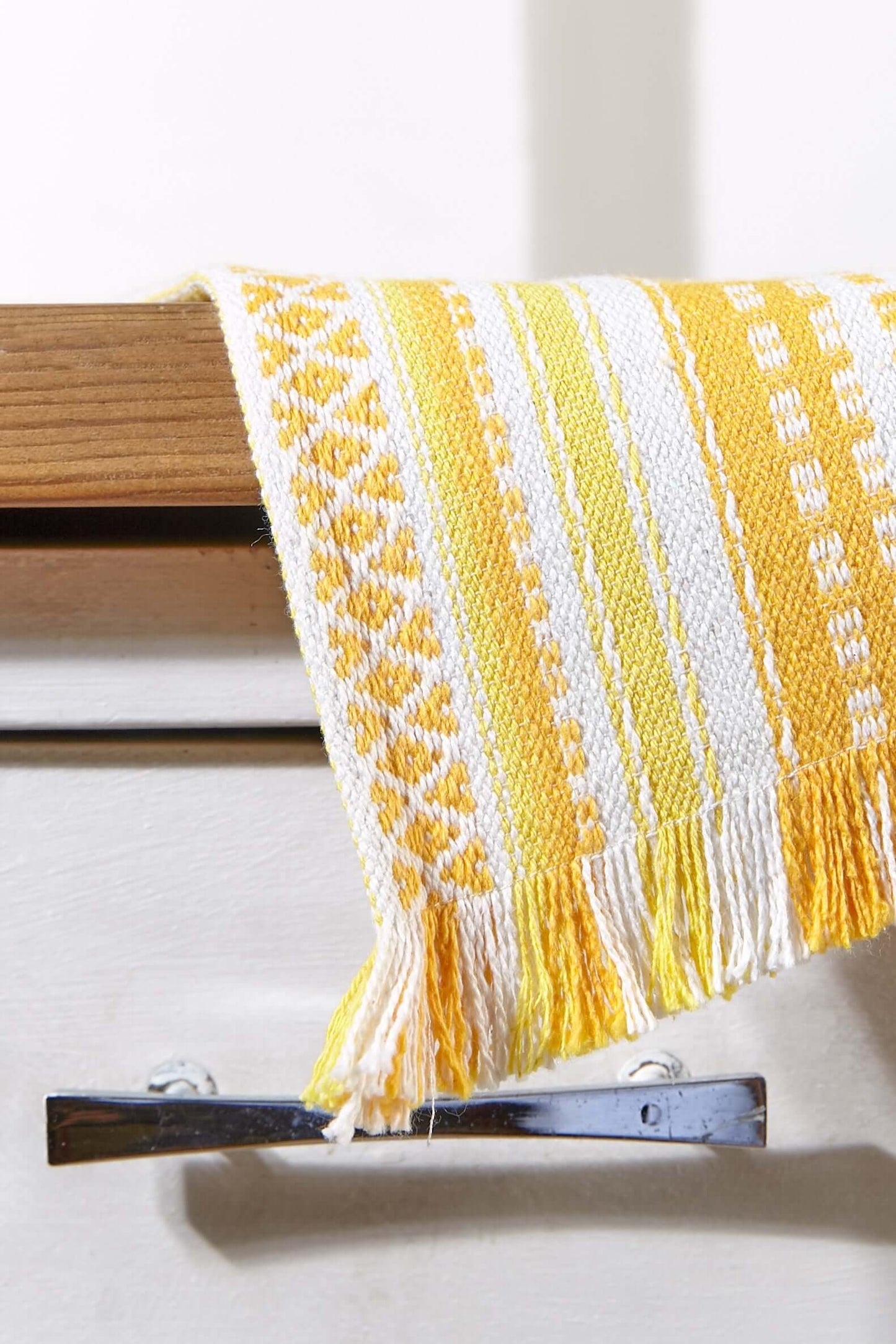 Camino de mesa tejido en amarillo y blanco, con motivos geométricos, textura rústica y flecos en los extremos.