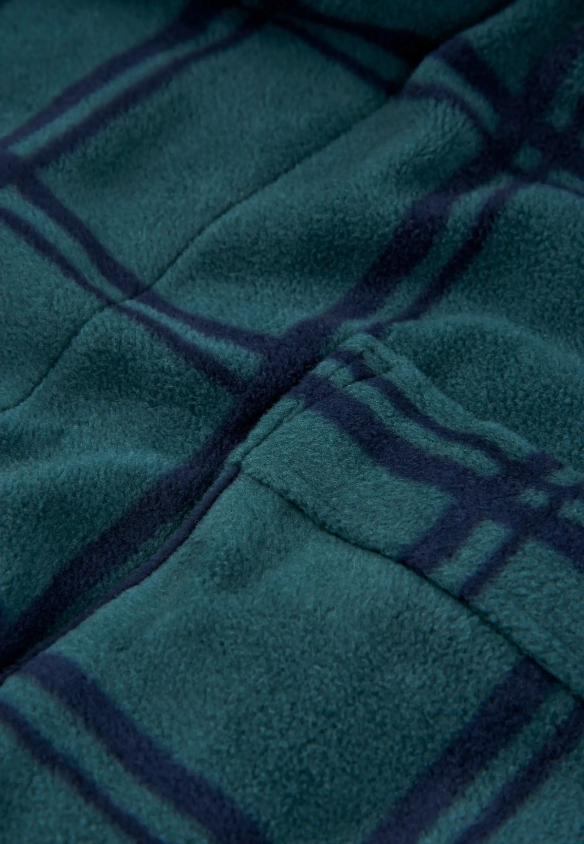 Detalle de bata polar verde con estampado de cuadros azul oscuro, tejido suave y costuras visibles.