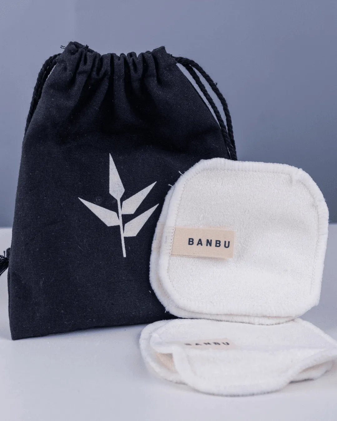 Discos desmaquillantes reutilizables blancos y suaves con etiqueta Banbu, junto a una bolsa negra de algodón orgánico.