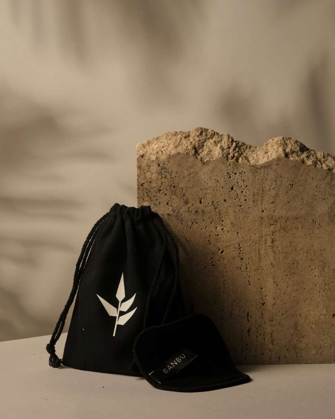 Bolsa y discos desmaquillantes negros Banbu de tela suave junto a una piedra texturizada en un ambiente natural.