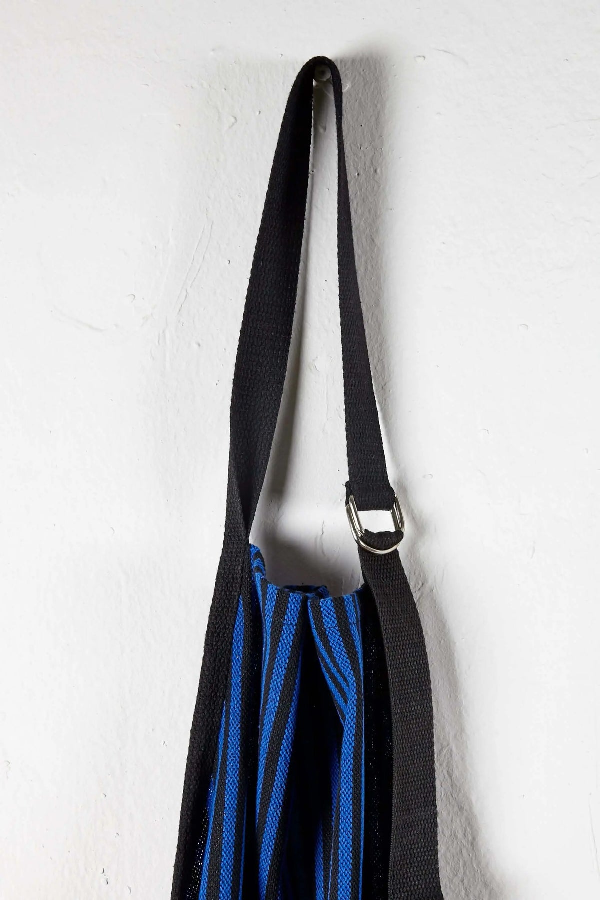 Delantal de loneta a rayas azules y negras, con cinta ajustable y hebilla metálica, colgado sobre pared blanca.