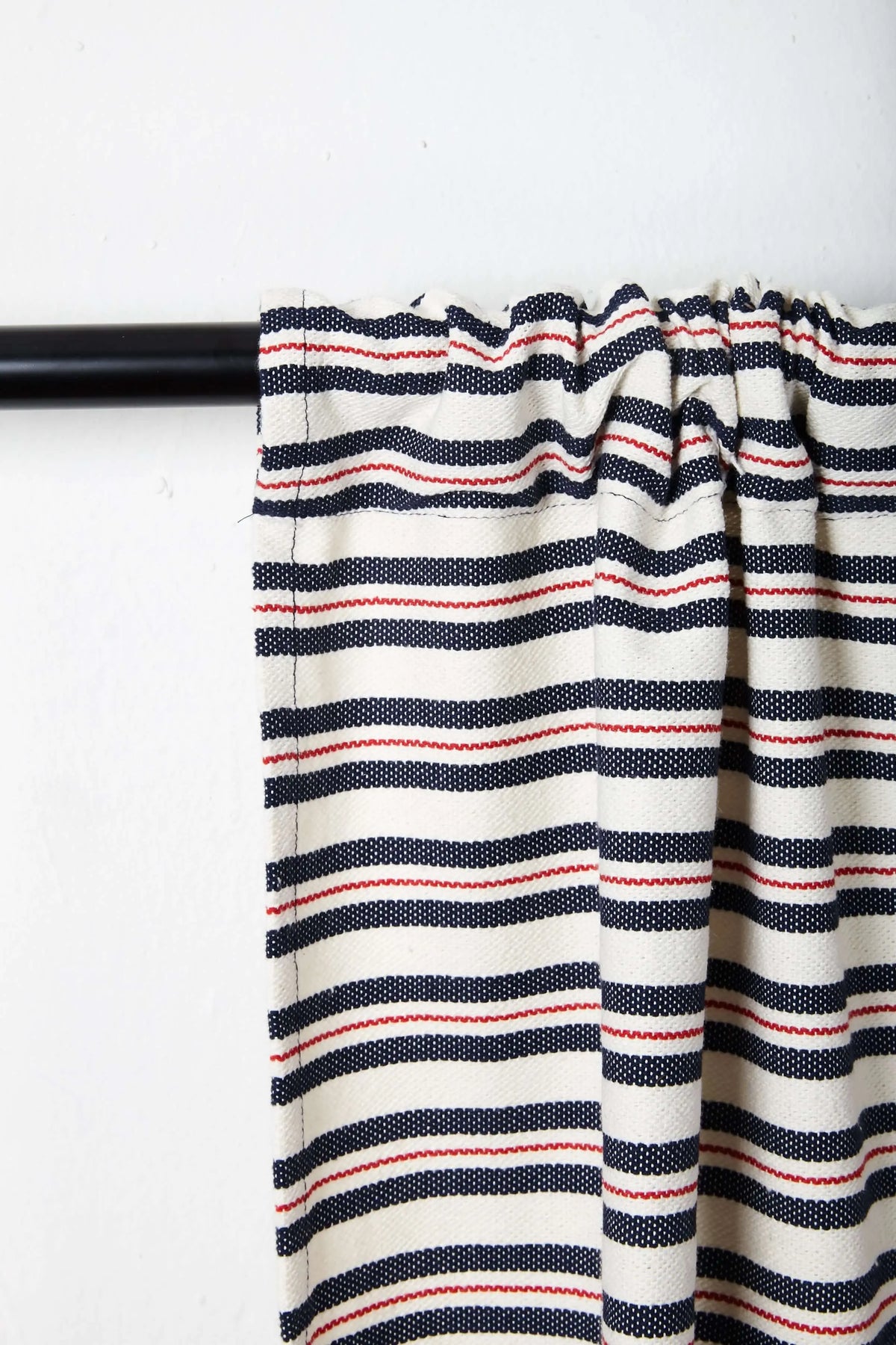 Off-white canvas curtain with horizontal navy blue and thin red stripes, gathered on a black rod.