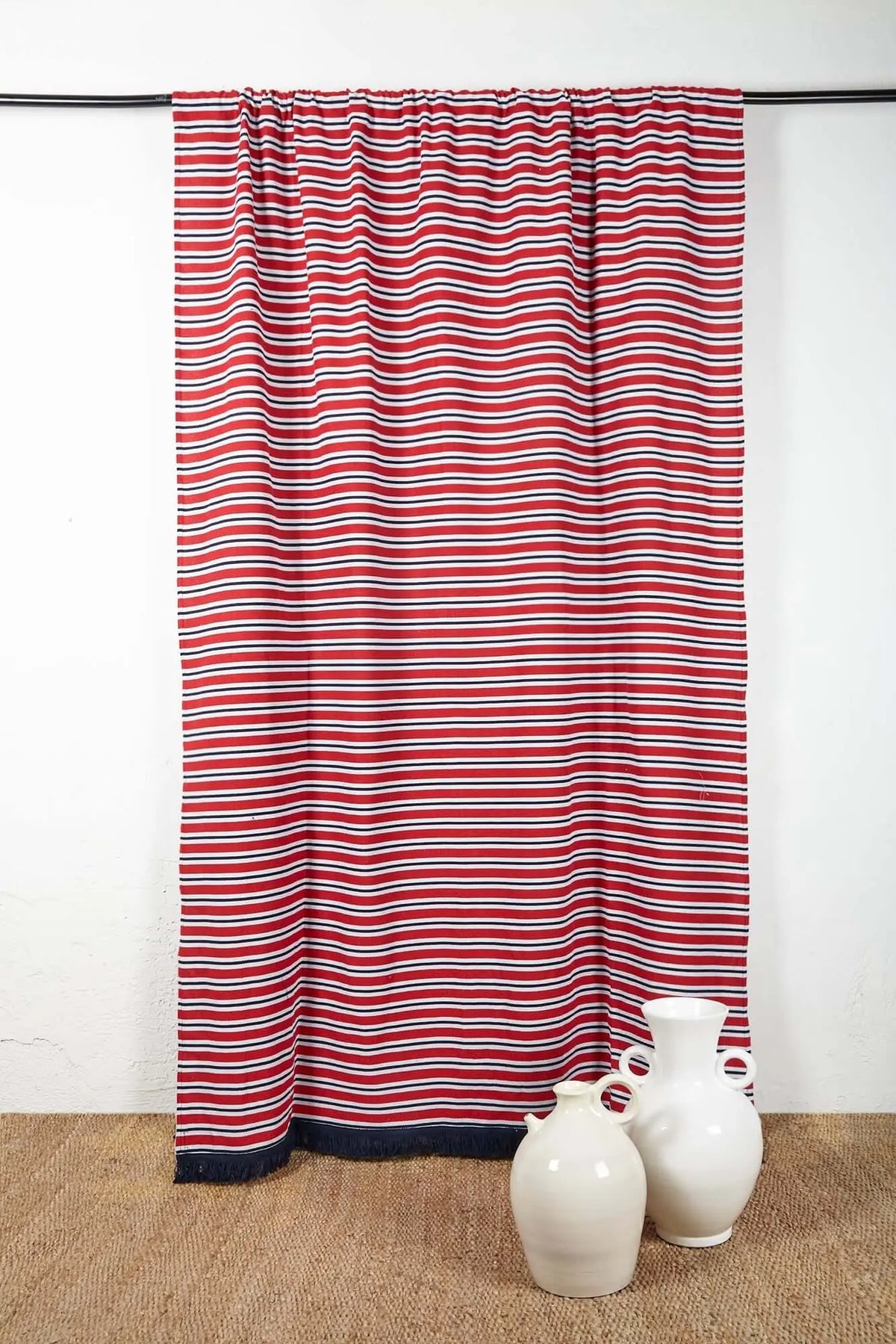 Red, white, and navy horizontal striped curtain with a dark blue fringed hem, hanging against a white wall.